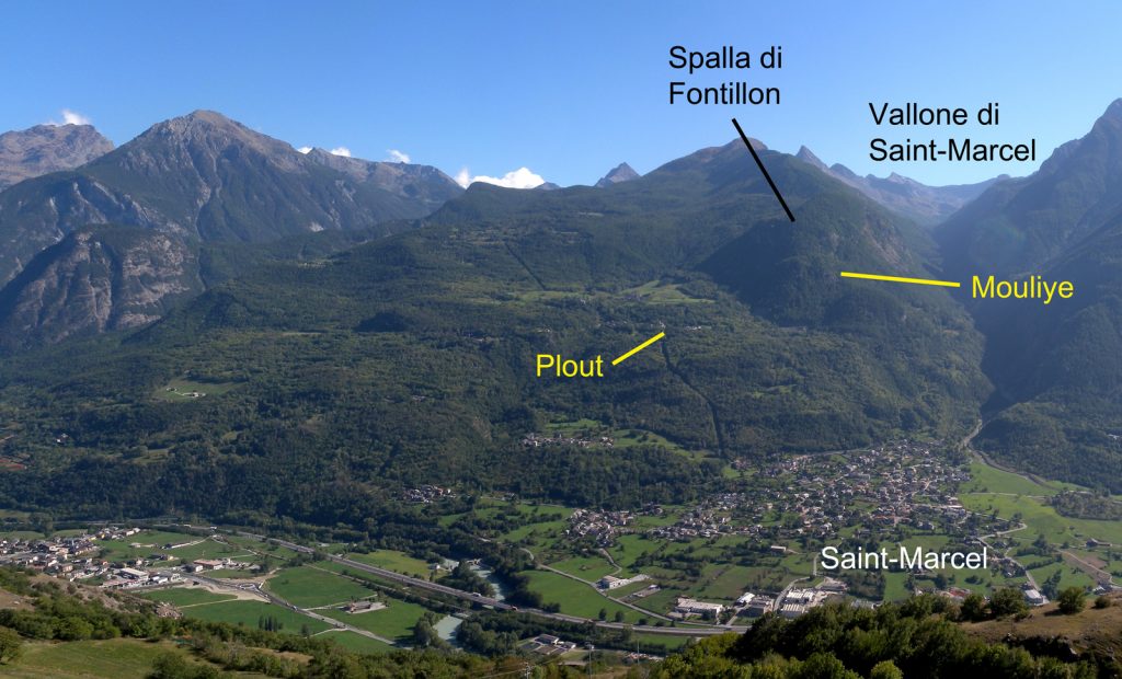 Veduta d'insieme della Collina di Saint-Marcel dal versante opposto della grande valle. Notare la forma rigonfiata verso il basso che traduce un rilascio del versante in dissesto. Il vasto cedimento lascia in piedi la spalla rocciosa di Fontillon, ai piedi della quale si svolge il nostro itinerario.